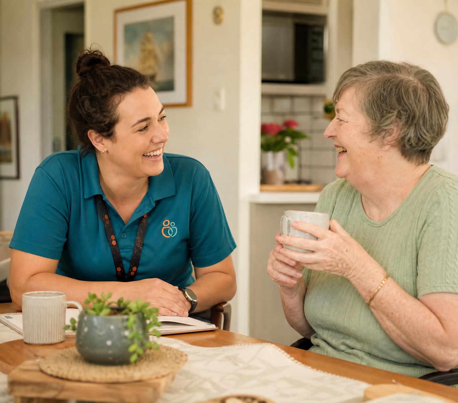 A support worker and a woman sharing a cup of tea and laughing together at a kitchen table